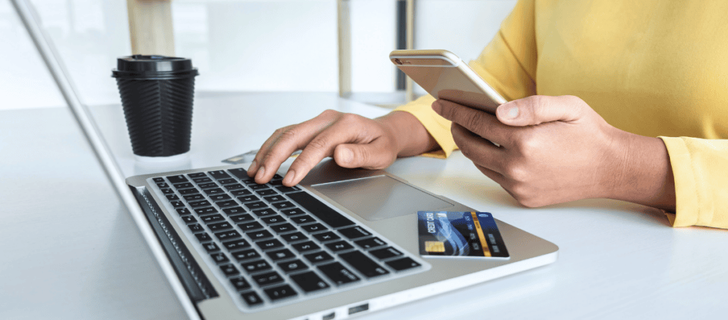 partial view of woman in yellow sweater with laptop computer, mobile phone and credit card shopping online and making a purchase to represent AI-referred shopping purchase blog topic