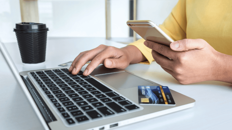 partial view of woman in yellow sweater with laptop computer, mobile phone and credit card shopping online and making a purchase to represent AI-referred shopping purchase blog topic