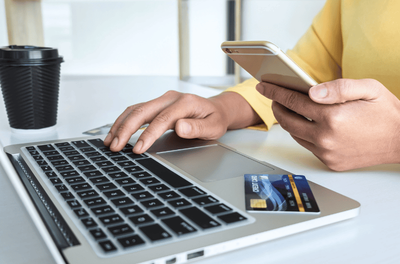 partial view of woman in yellow sweater with laptop computer, mobile phone and credit card shopping online and making a purchase to represent AI-referred shopping purchase blog topic